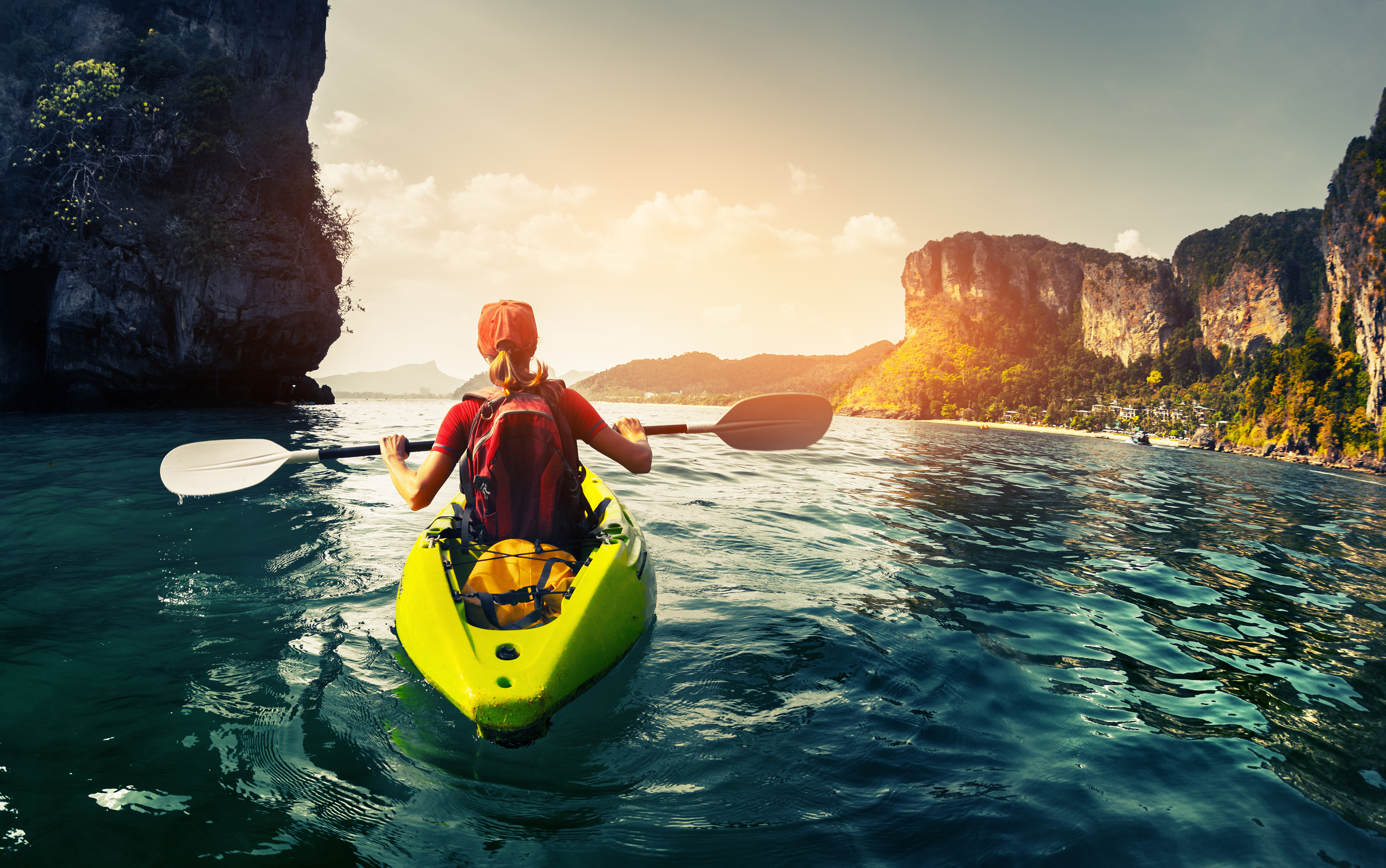Lady paddling the kayak in the calm tropical bay at sunset